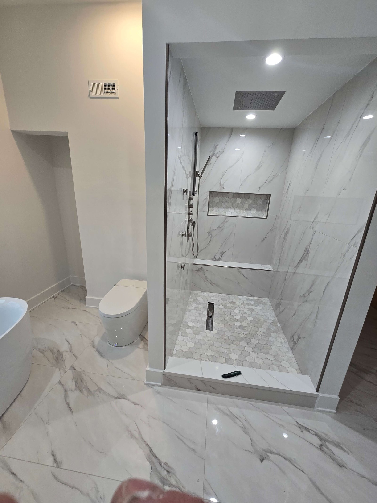 Finished walk-in shower with hex tile floor and niche